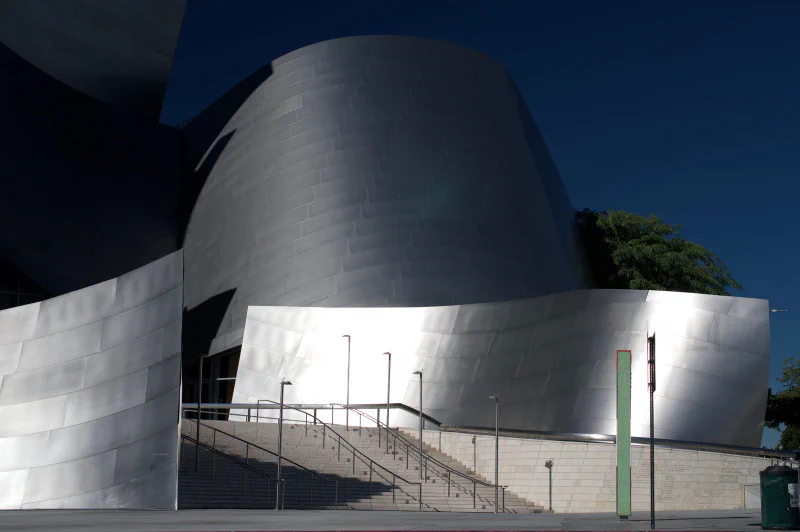 Walt Disney Concert Hall seen from street level on Grand Avenue, its steel curves above the public entrance staircase